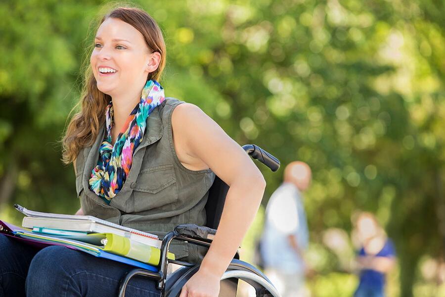 Young woman in wheel chair with books on her lap, outside on a nice day.